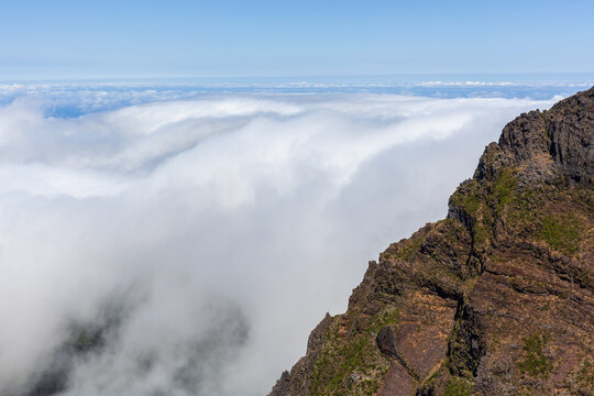Hiking trail winds along rocky cliffs. PR1 Vereda do Areeiro path on Madeira Island. Dramatic cloudy sky overlooks mountainous terrain.