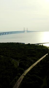 Vertical video. Oresund bridge. Drone footage of the cable-stayed span connecting Sweden and Denmark, its two-level road and rail structure reaching toward the horizon over calm water at sunset.. Dro
