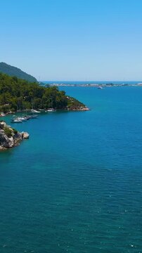 Vertical video. Marmaris, Turkey. Aerial drone view over a deeply indented fjord-like bay, where forested mountains plunge into turquoise Mediterranean water, clear summer sky. Aerial View. Rich colo