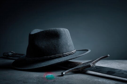 Black fedora hat and sharp medieval sword on dark textured surface
