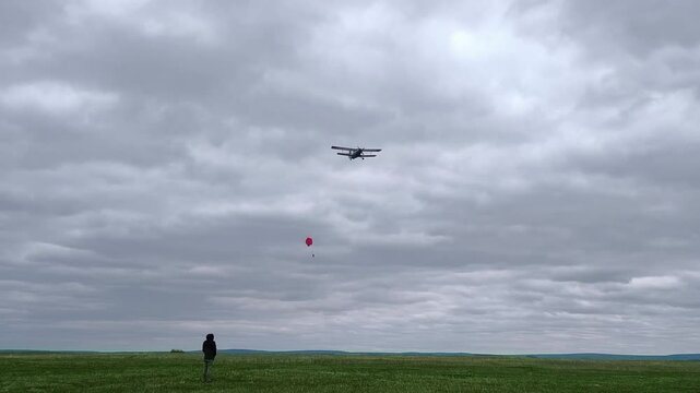 An airplane parachutes cargo over an open field under an overcast sky, a shot of aviation tests and delivery.
