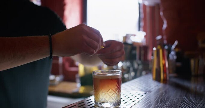 Refreshing cocktail. Classic beverage. Bartender man serving crystal glass garnished with lemon spiral zest red cherry on bar counter.
