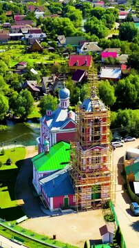 Vertical video. Pereslavl-Zalessky, Russia. Church of the Forty Martyrs of Sebastia, pink baroque walls and green rooftops with scaffolding on the bell tower, Drone footage over the Trubezh River and