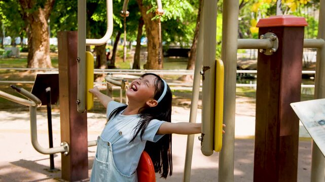 Young Asian Girl Laughing While Playing on Outdoor Fitness Equipment