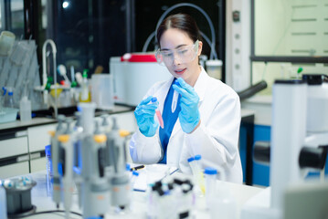 Fototapeta premium Young Asian scientist analyzing samples with microscope in a modern laboratory, focusing on medical research, biotechnology, healthcare, and innovation.
