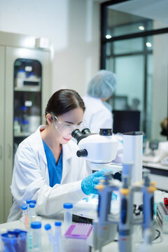 Young Asian scientist analyzing samples with microscope in a modern laboratory, focusing on medical research, biotechnology, healthcare, and innovation.