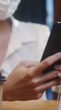 Vertical Screen : Young Asia female wear face mask self service use mobile phone pay contactless at restaurant. Girl barista talking receive order from customer at cafe. Lifestyle after corona virus.