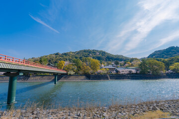 Fototapeta premium Beautiful scenic view of Uji River flowing through Uji city in Kyoto, Japan, during spring season with blooming cherry blossom trees, surrounded by green mountains under a bright clear sky.