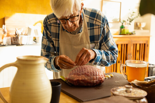 elderly man in light filled kitchen preparing a pot roast 