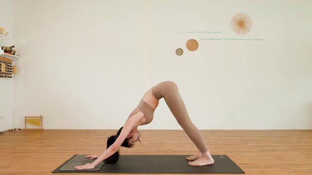Asian Woman Performs Three Legged Downward Dog Yoga Pose in Studio