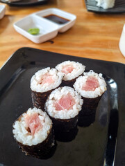 A top-down, high-angle shot of five pieces of tuna maki sushi arranged on a glossy black square plate © awgraphoto