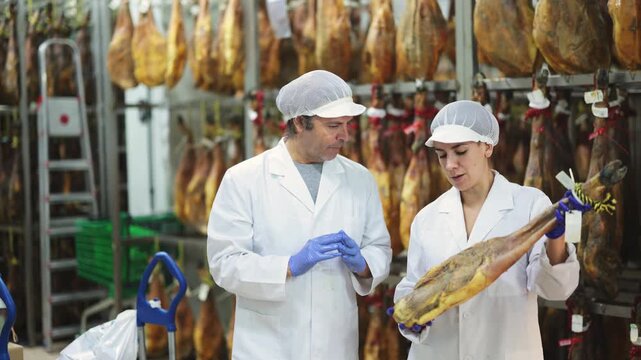 Two factory employees inspect the hanging jamon, they discuss the quality of the product. High quality 4k footage