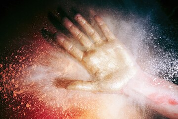 Fototapeta premium Gold painted hand with exploding colorful powder particles on a dark surface for festive celebrations, creative art campaigns and cultural event advertising