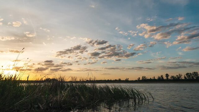 Sunset over a lake with beautiful clouds, timelapse of quickly flying clouds in the sky and the setting sun behind the horizon