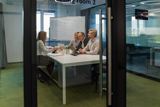 A view through a glass partition shows a modern, busy office interior. Job interview process is in office. Human resources, meeting and group of hiring candidates for vacancy