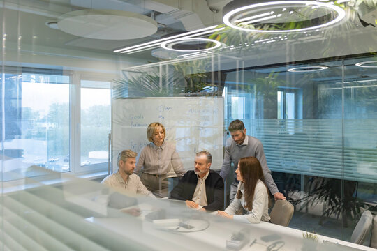 A modern office interior, featuring a blurred view of workers at desks, through a glass partition.