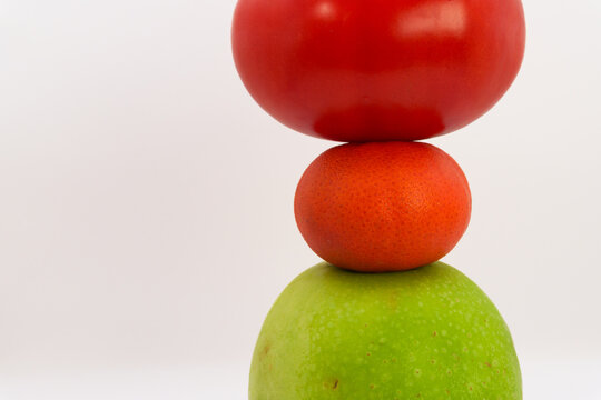 Mandarin, apple, tomato and sweet pepper in the form of a tower on a white background, the concept of healthy eating from fruits and vegetables, health care, fruit diet, vegans and vegetables. High qu
