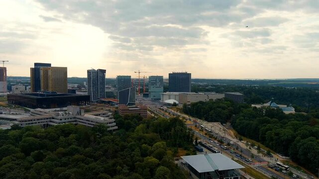 Luxembourg City, Luxembourg. The Kirchberg Plateau skyline, a sweeping Drone footage over the European quarter's modern high-rise towers and glass facades set against a partly cloudy sky at dusk. Dro