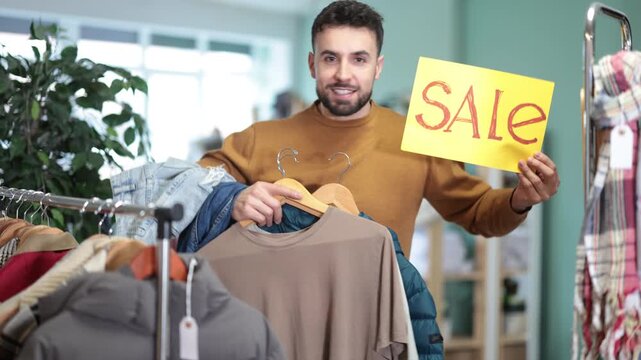 Man with poster in hands announces SALE. Closing of season and price reduction in family clothing store, closing of season, record price reduction, liquidation of collection