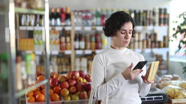 Adult woman buyer scanning qr code for fresh cheese in grocery store