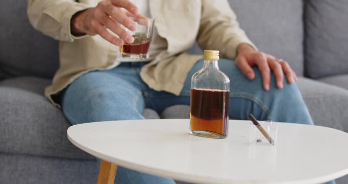 Alcohol and whiskey bottle near man signals addiction. Scene shows a man at home with glass and bottle, implying stress, depression, risk, and coping. Clear concept of alcohol abuse and harm.