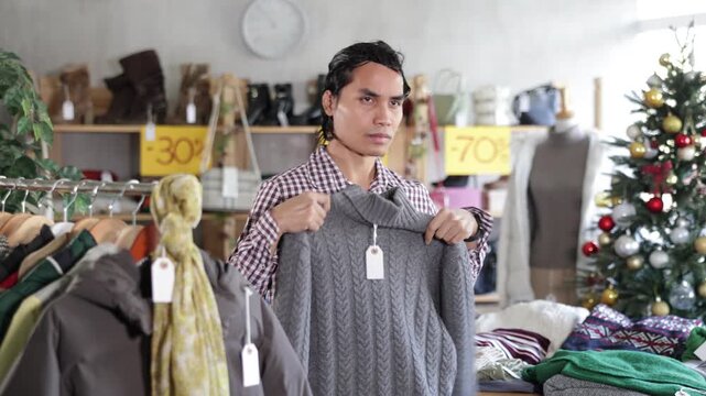In chain shop, Indonesian man choose sweater, X mas shopping. Changing wardrobe, shaping style of clothing. Designer clothes, clothing of world brands. 