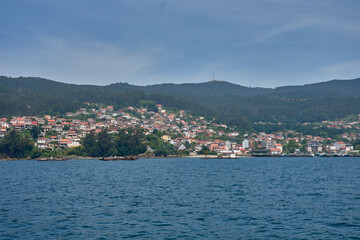 Fototapeta premium Small coastal houses integrated into the green landscape of the Vigo estuary, photographed from the sea