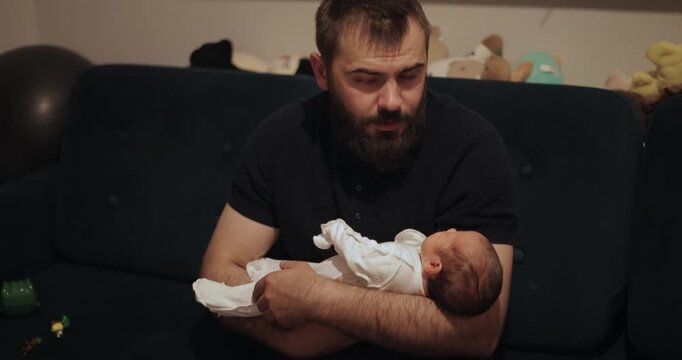 Father cradling newborn infant on living room sofa at night and holding baby, fatherhood lifestyle moment.