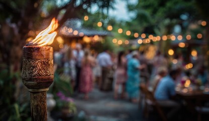 Naklejka premium Tiki torch with flickering flame in the foreground during an outdoor gathering with people at dusk, illuminated by string lights in a festive setting