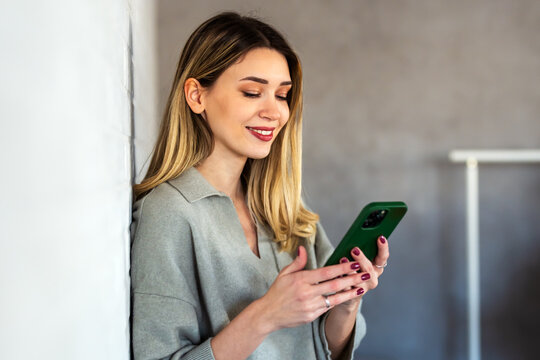 Smiling young woman chatting in social networks, working, using mobile applications at home.