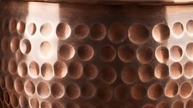 Closeup of Hammered Copper Pot Surface with Reflective Light Patterns.