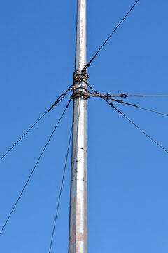 A detailed close up view of a metal tram line utility pole with steel guy wires and tensioners against a clear blue sky