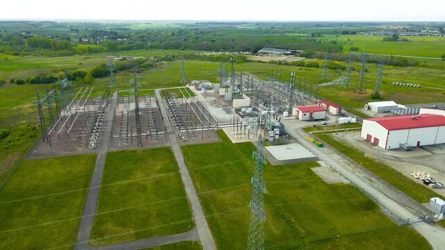 Electrical Substation Aerial View Showing High Voltage Transformers, Pylons and Power Lines Surrounded by Countryside