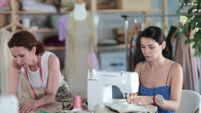 Woman tailor draw dress pattern with curve ruler on paper, female master seamstress sewing cloth with sewing machine. Tailor workplace with cut textile, sewing machine, thread, pins, needles, tape