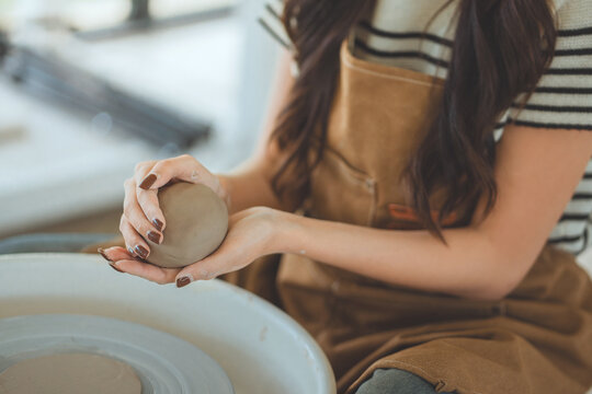 Close up of female artisan hands shaping raw clay ball on pottery wheel inside studio creative woman craftsman making ceramic pot pottery class and traditional handicraft hobby concept