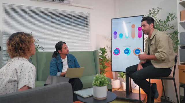 A professional East Asian business woman gestures actively while leading a tech presentation about an AI Assistant system on a vertical monitor, as her multiethnic male colleagues hold a laptop 
