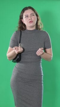 Young woman stands against green screen, touching head and looking puzzled, she forgot something important