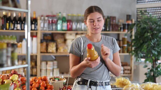 Young woman chooses natural peach juice in a supermarket. Customer holds glass bottle of peach juice with pulp in her hand. High quality 4k footage