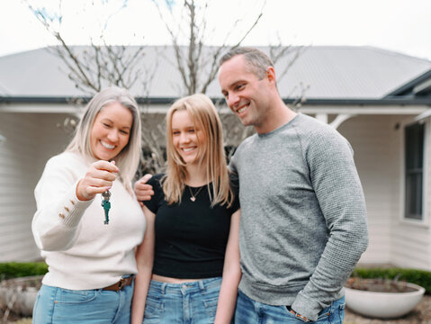 Happy family standing in front yard with mum holding out the key of their new home