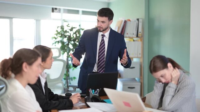 Angry young male manager standing and scolding colleagues during a stressful corporate meeting. High quality 4k footage