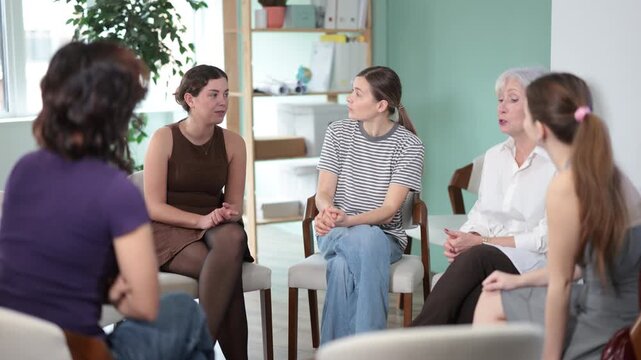 Focused female colleagues of different ages friendly talking while sitting in circle on chairs, psychological support in big office 