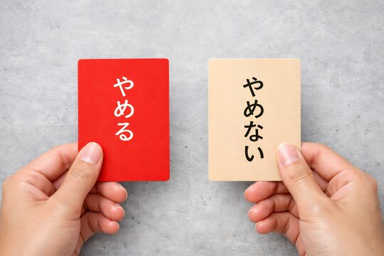 やめるかやめないか選択を迫られ赤とベージュのカードを持ち悩む日本人の手元