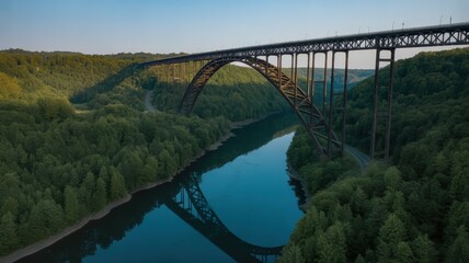 Fototapeta premium Massive steel arch bridge over a wide river surrounded by lush green forests