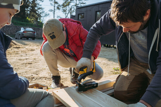 A man and children construct a tall raised garden bed from larch wood, using a cordless drill and pocket hole jig during assembly