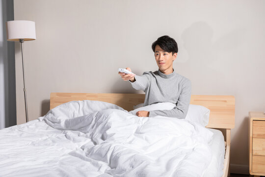 Young man in bed using remote control at home