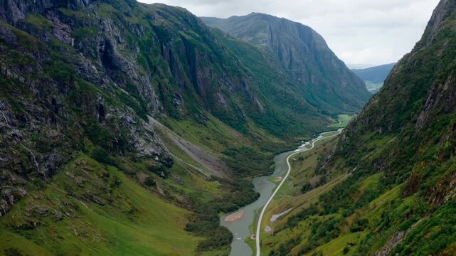 High aerial drone footage of an empty winding road next to a river flowing through a deep mountain canyon in Klakegg, Norway. Epic summer wilderness landscape for indie travel and wild tourism
