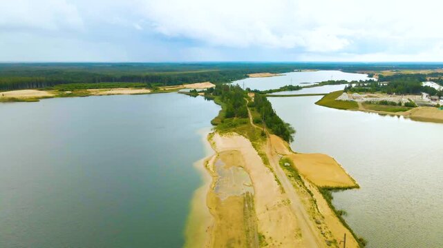 Stunning aerial perspective of a sand quarry featuring flooded pits that form artificial lakes, with a sandy road bisecting the water