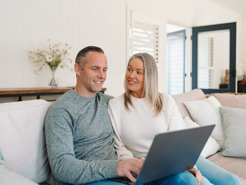 Happy couple looking at the laptop screen while sitting on the couch in the living room