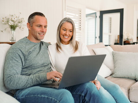 Happy couple looking at the laptop screen while sitting on the couch in the living room