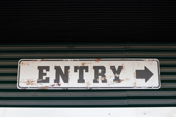 Obraz premium worn out entry word sign on the wall with arrow pointing to right outdoors